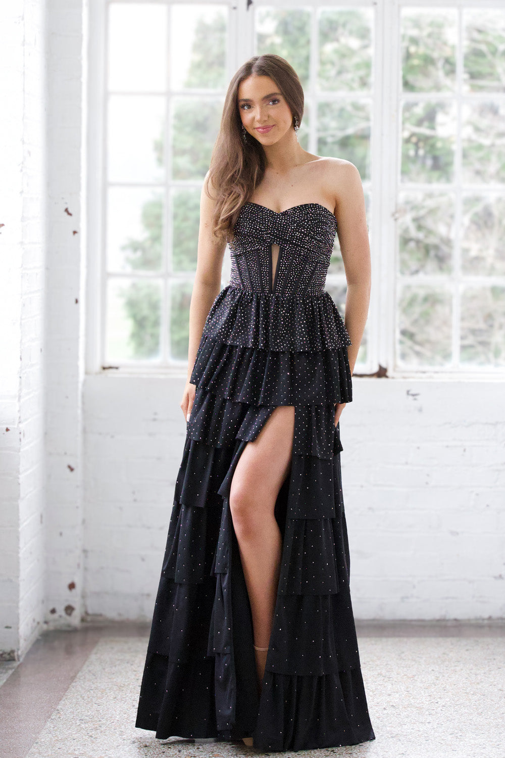 Miah Vega 24602 Black tiered prom dress with a high slit and sparkling embellishments.