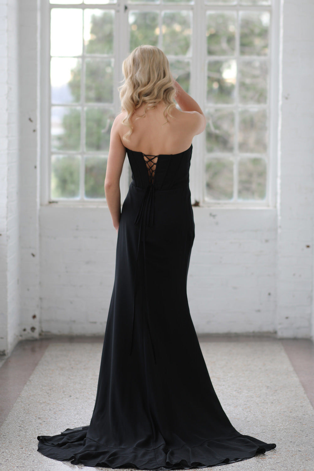 Miah Vega 24603 Black mermaid prom dress with a lace-up back and elegant train, back view.