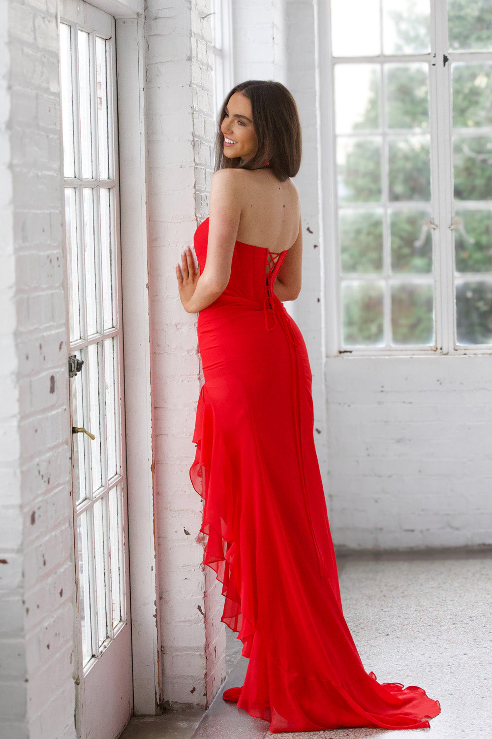 Miah Vega 24603 Red mermaid prom dress with a lace-up back and flowing ruffle detail.
