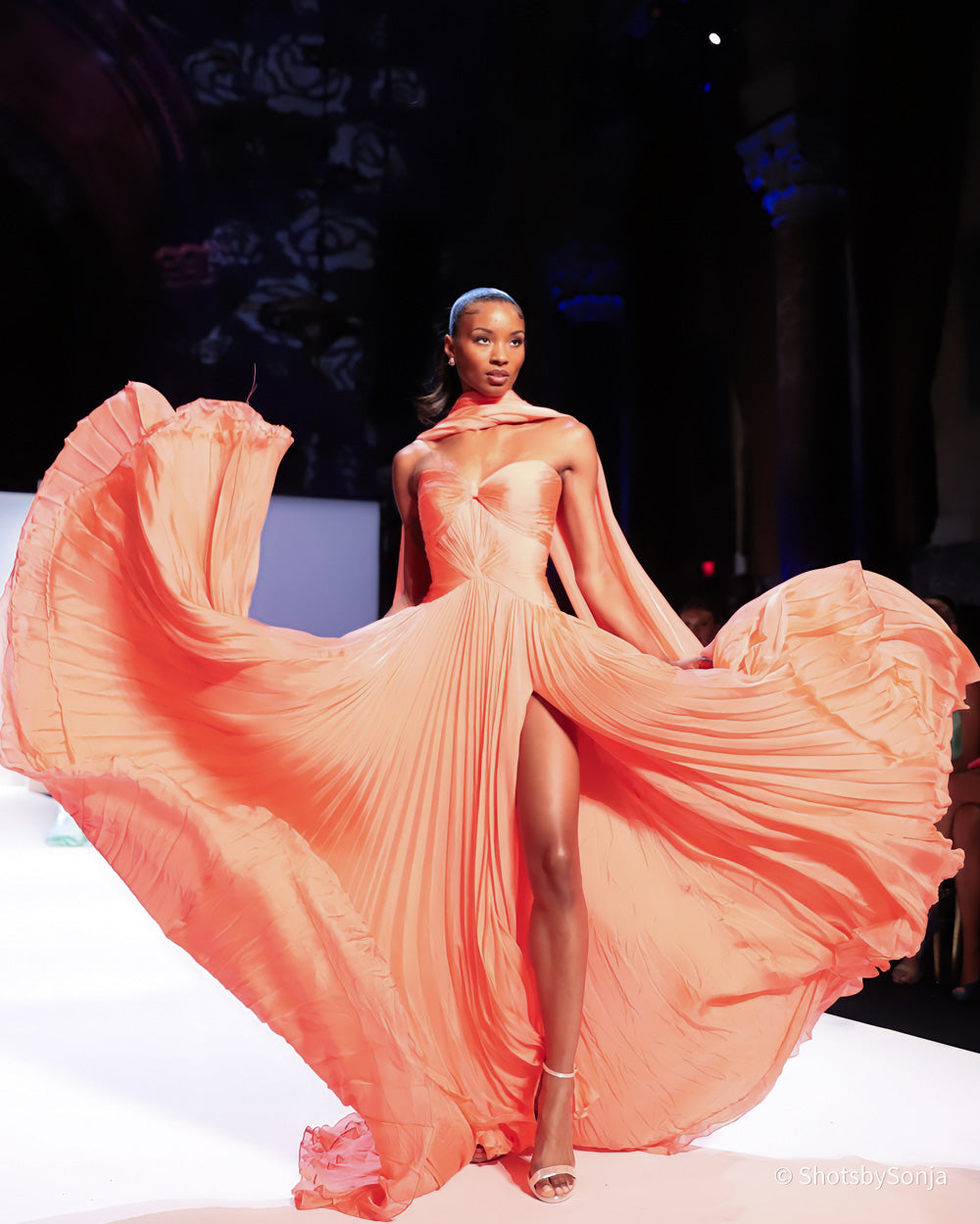 Sherri Hill 46715 coral couture gown with billowing pleated skirt dramatically fanned open in motion on runway