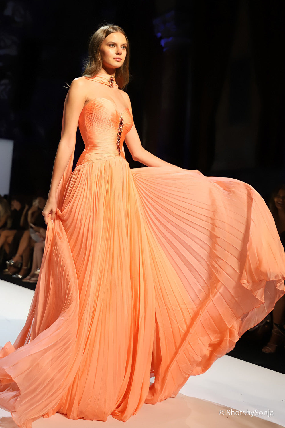 Sherri Hill 46759 coral couture gown with flowing pleated skirt and draped halter neckline in motion