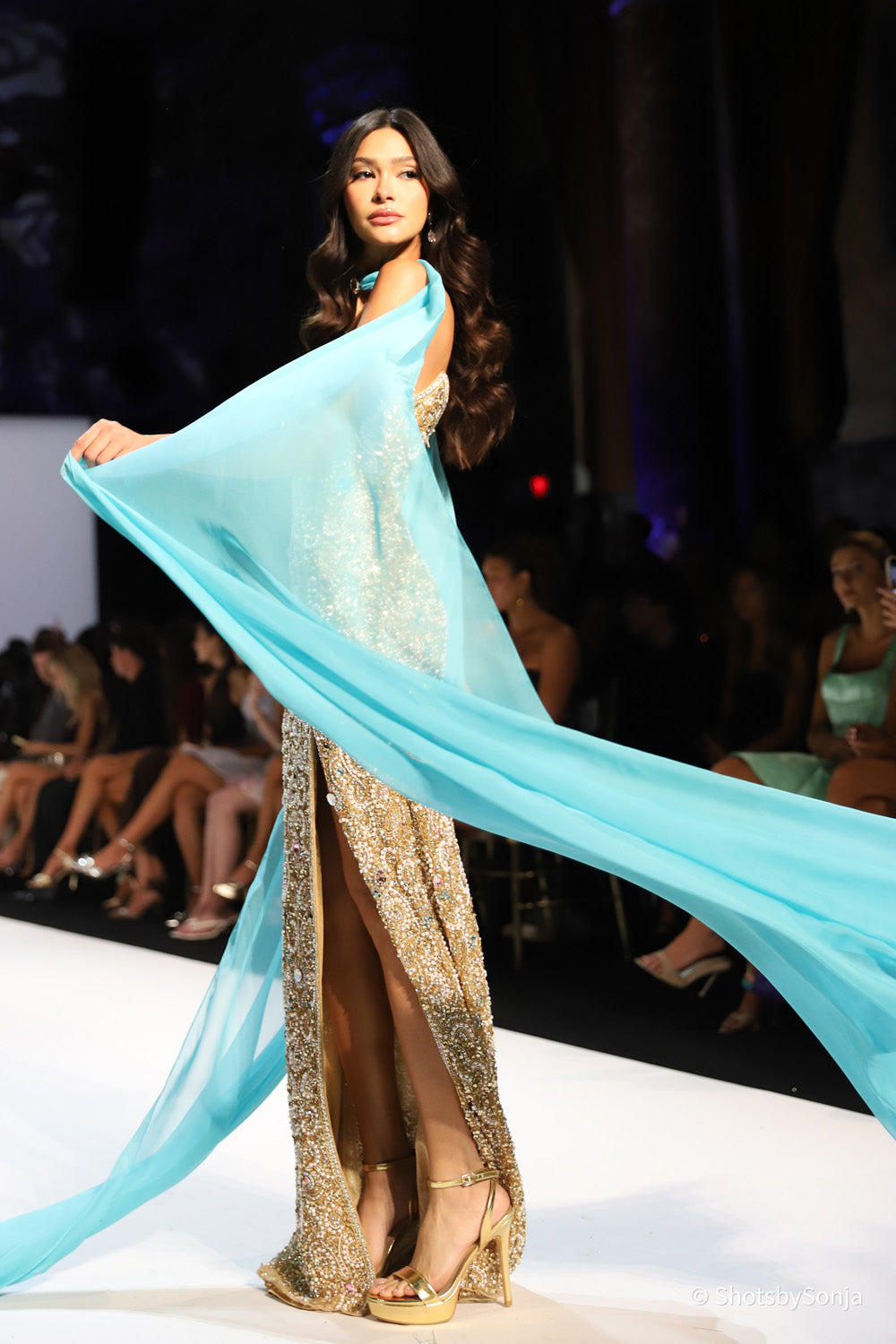 Sherri Hill 67348 gold beaded mermaid gown with aqua chiffon cape panel flowing behind showing leg slit detail