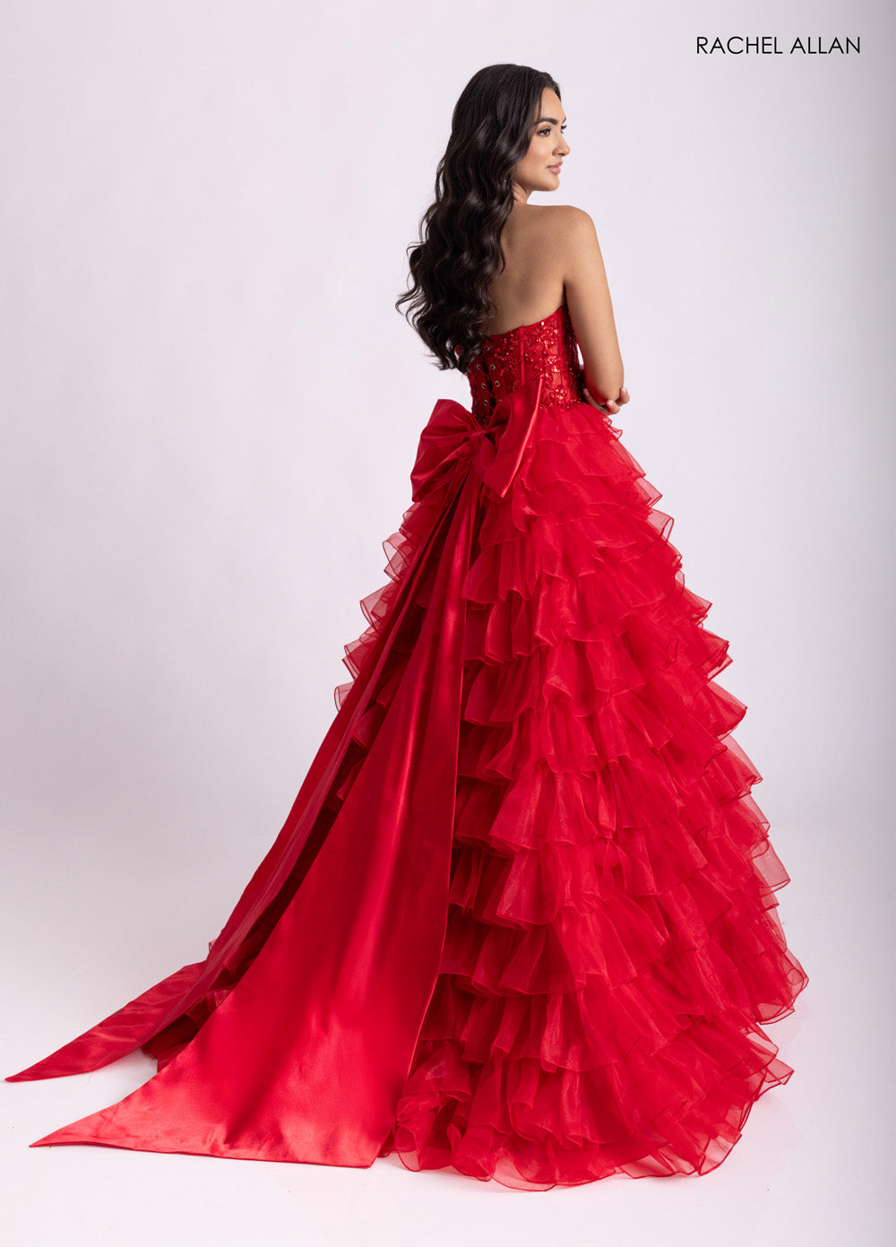 Rachel Allan 71006 Red ballgown with ruffled layers and a large bow, showcasing a stunning back view prom dress.