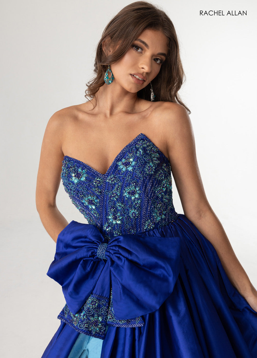 Rachel Allan 71068 Royal turquoise prom dress with beading and a large bow, featuring a fitted bodice.