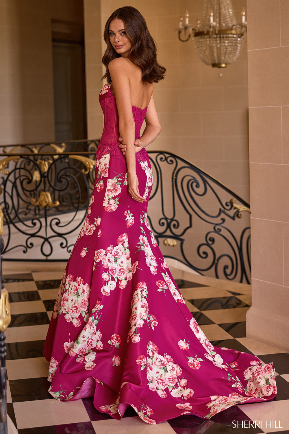 Sherri Hill 58180 plum rose-print trumpet skirt with dramatic train and open lace corset back, rear three-quarter view.