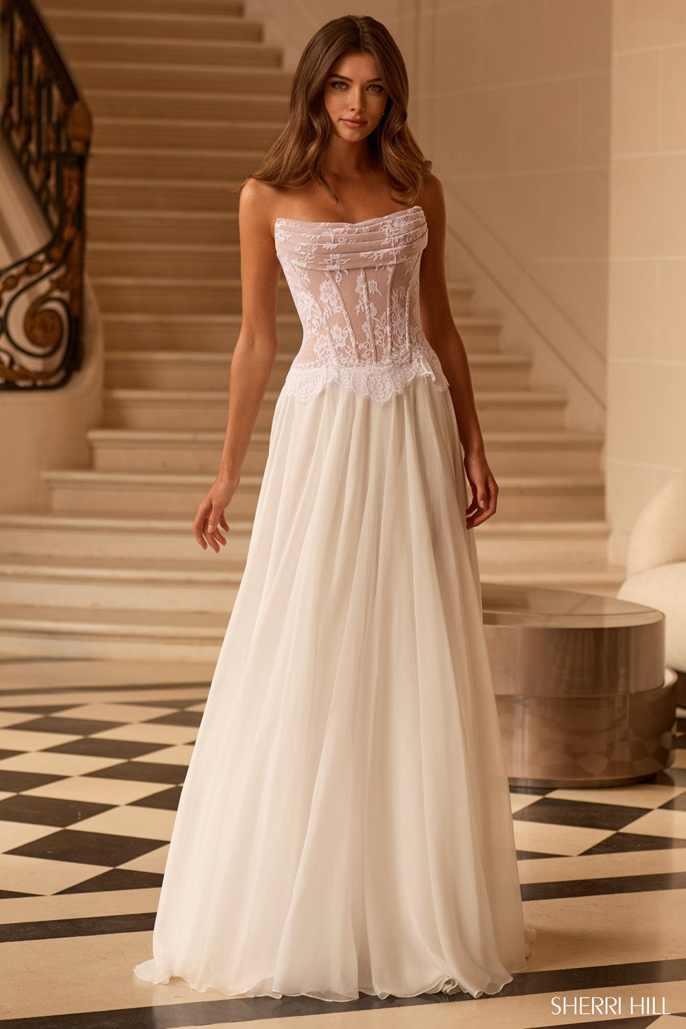 Sherri Hill 58248 in Ivory Nude, front view, sheer lace corset bodice and flowing A-line chiffon skirt, grand staircase setting.