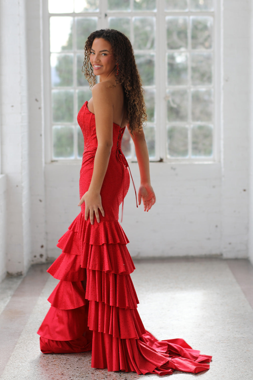 Miah Vega 24606 Red mermaid prom dress with ruffled layers and lace-up back, side view.