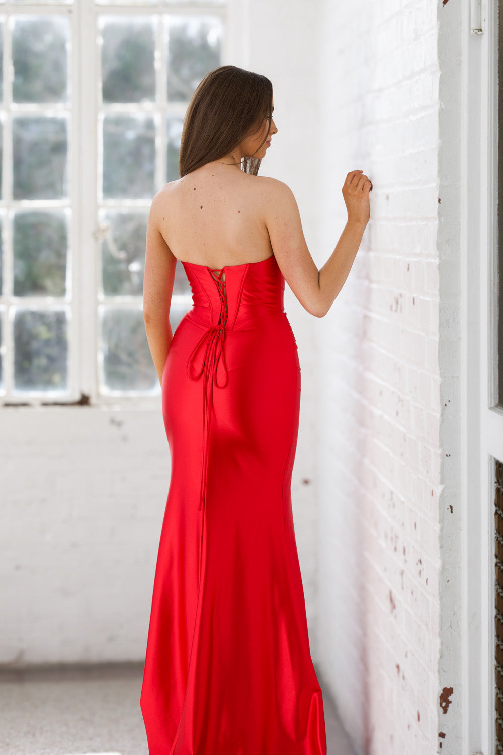 Miah Vega 24608 Red mermaid prom dress with a lace-up back and side slit, back view.