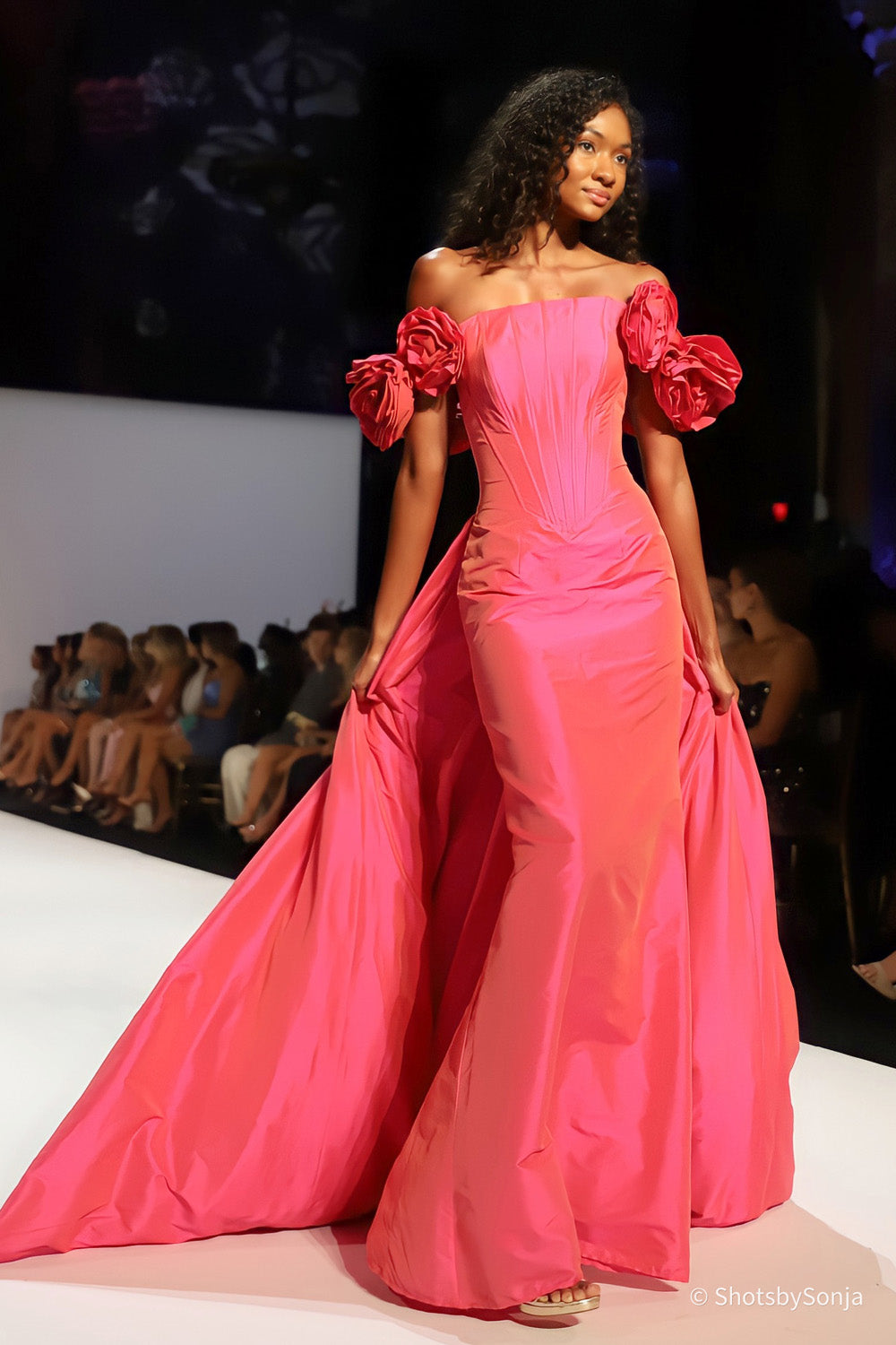 Sherri Hill 67309 coral taffeta off shoulder ballgown with sculptural rose sleeves model holding overskirt