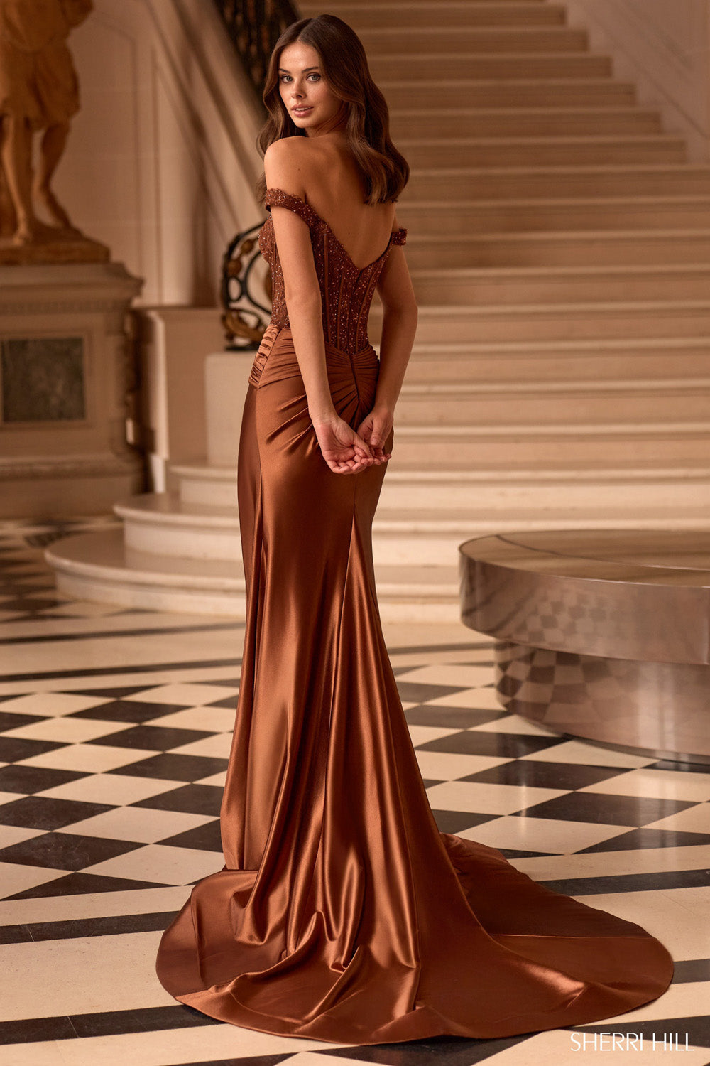 Sherri Hill 58042 in brown, back view showing beaded off-shoulder corset, ruched waist, and mermaid train on marble staircase.