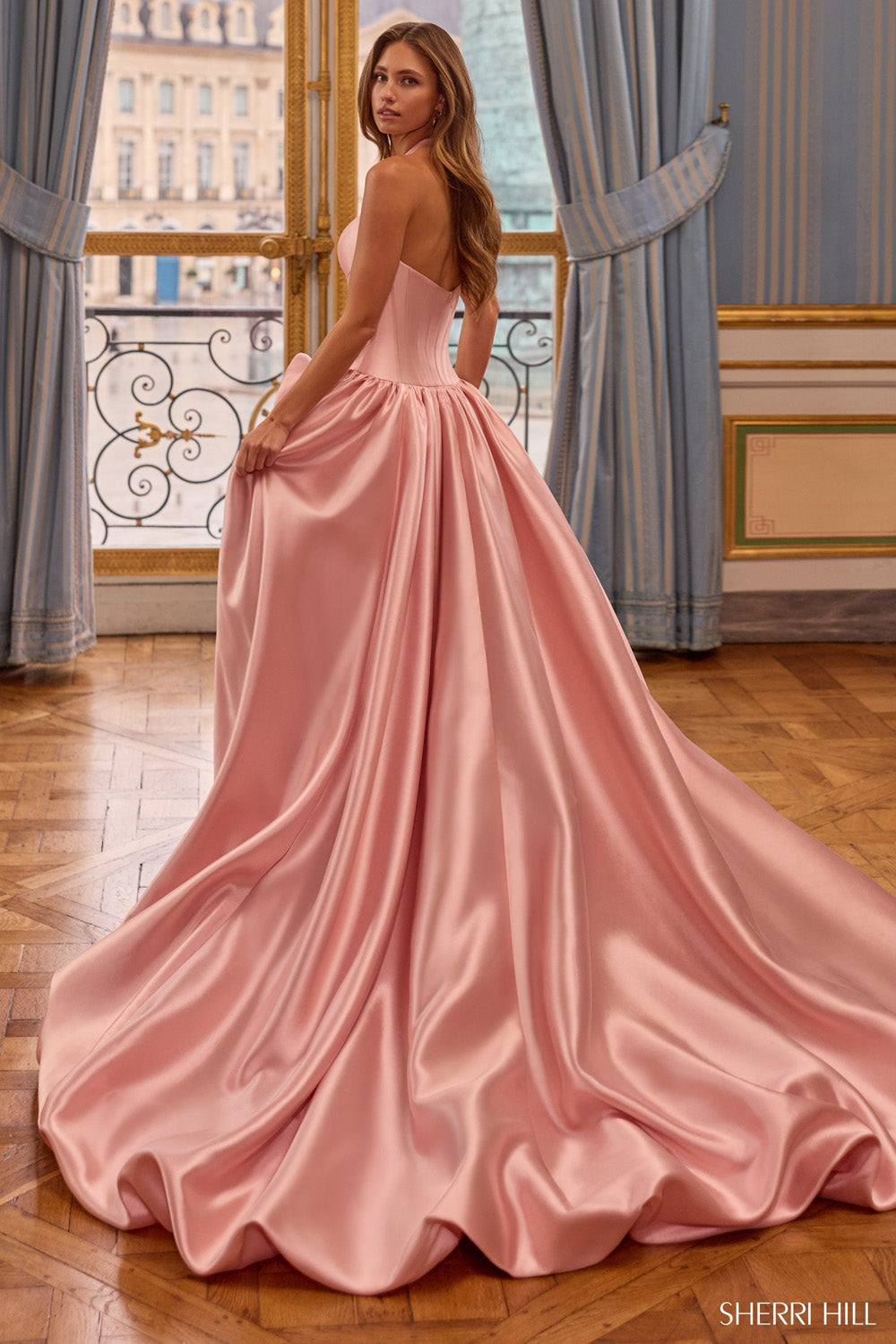 Sherri Hill 58162 back view in blush satin — open halter back, structured corset waist, and sweeping floor-length train in ornate interior.