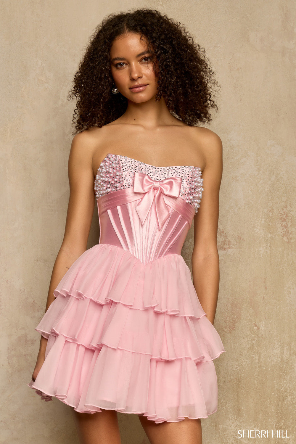 Front view of Sherri Hill 58176 light pink strapless corset dress with pearl rhinestone trim, satin bow, and ruffled mini skirt.