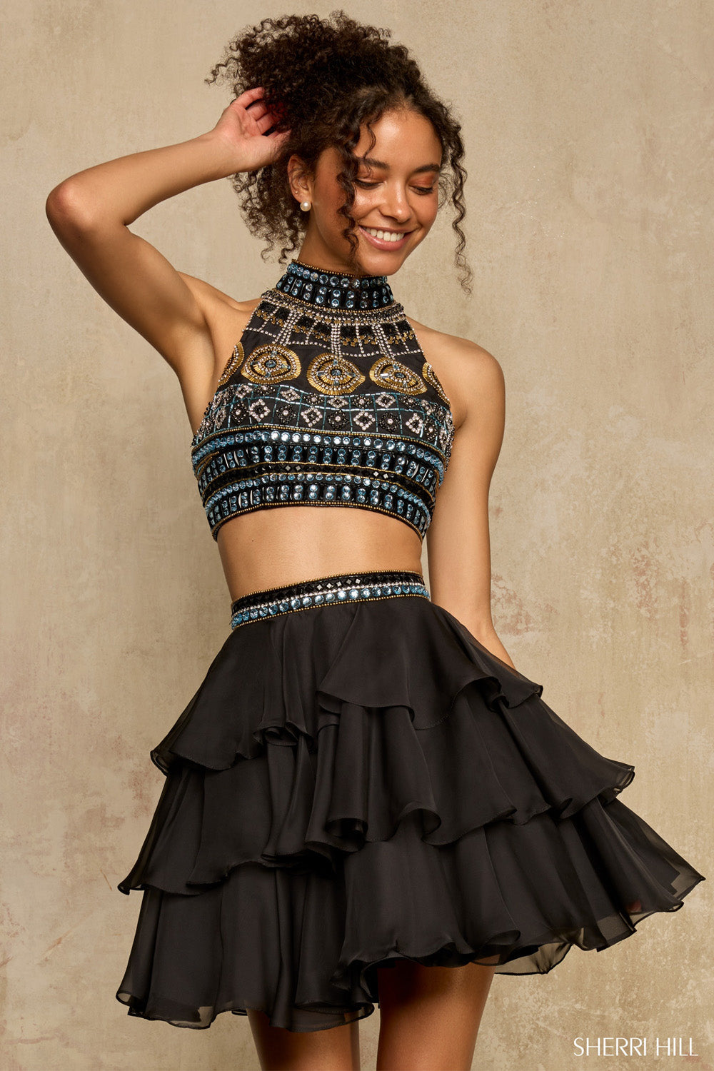 Sherri Hill 58399 black two-piece homecoming dress, beaded halter crop top and tiered chiffon skirt, smiling model, front view